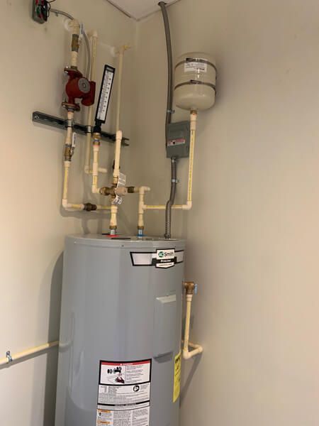 A gray AO Smith water heater with attached pipes, a red pump, and a small expansion tank mounted on a beige wall.