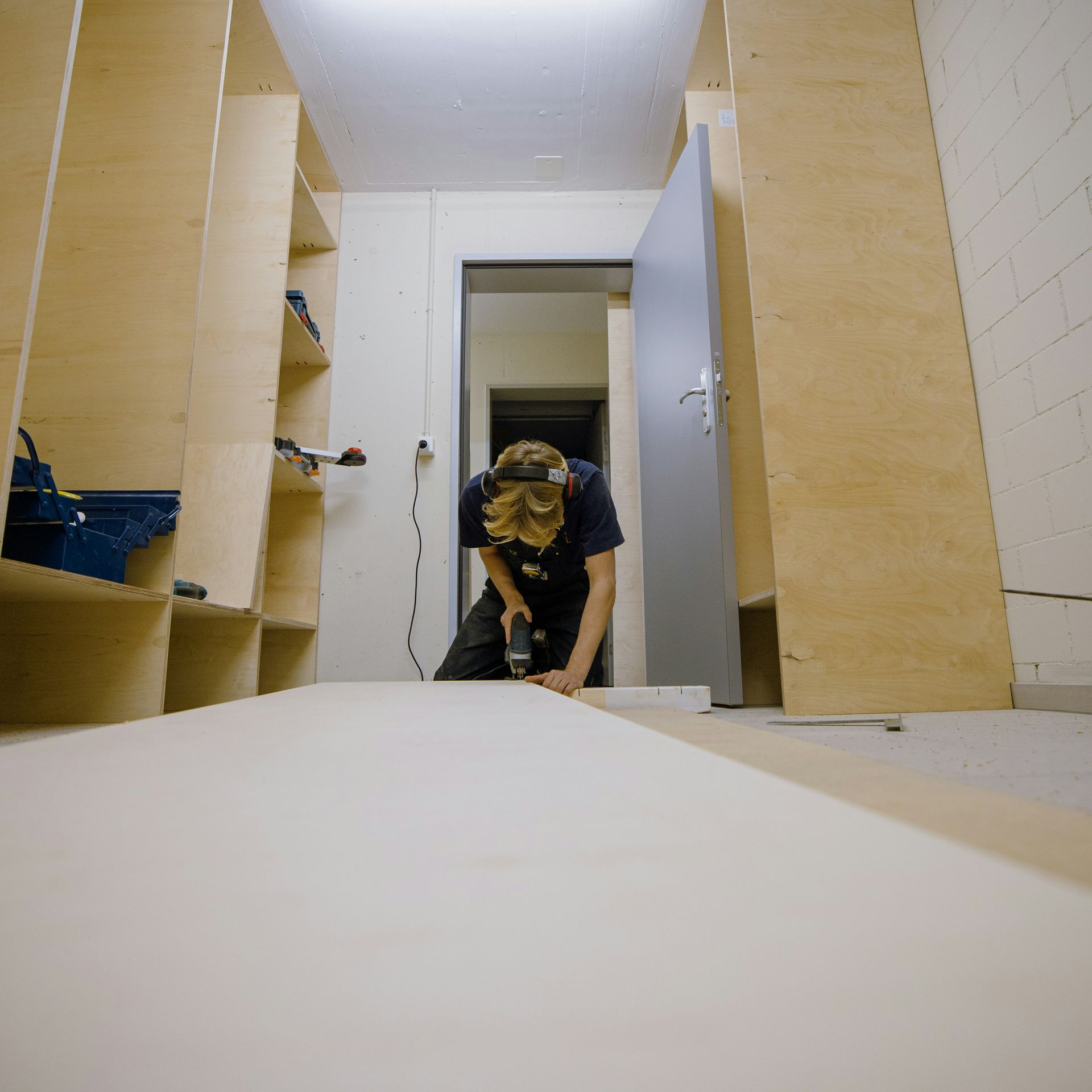 Person crouching on the floor in a narrow white room, working near an open doorway.