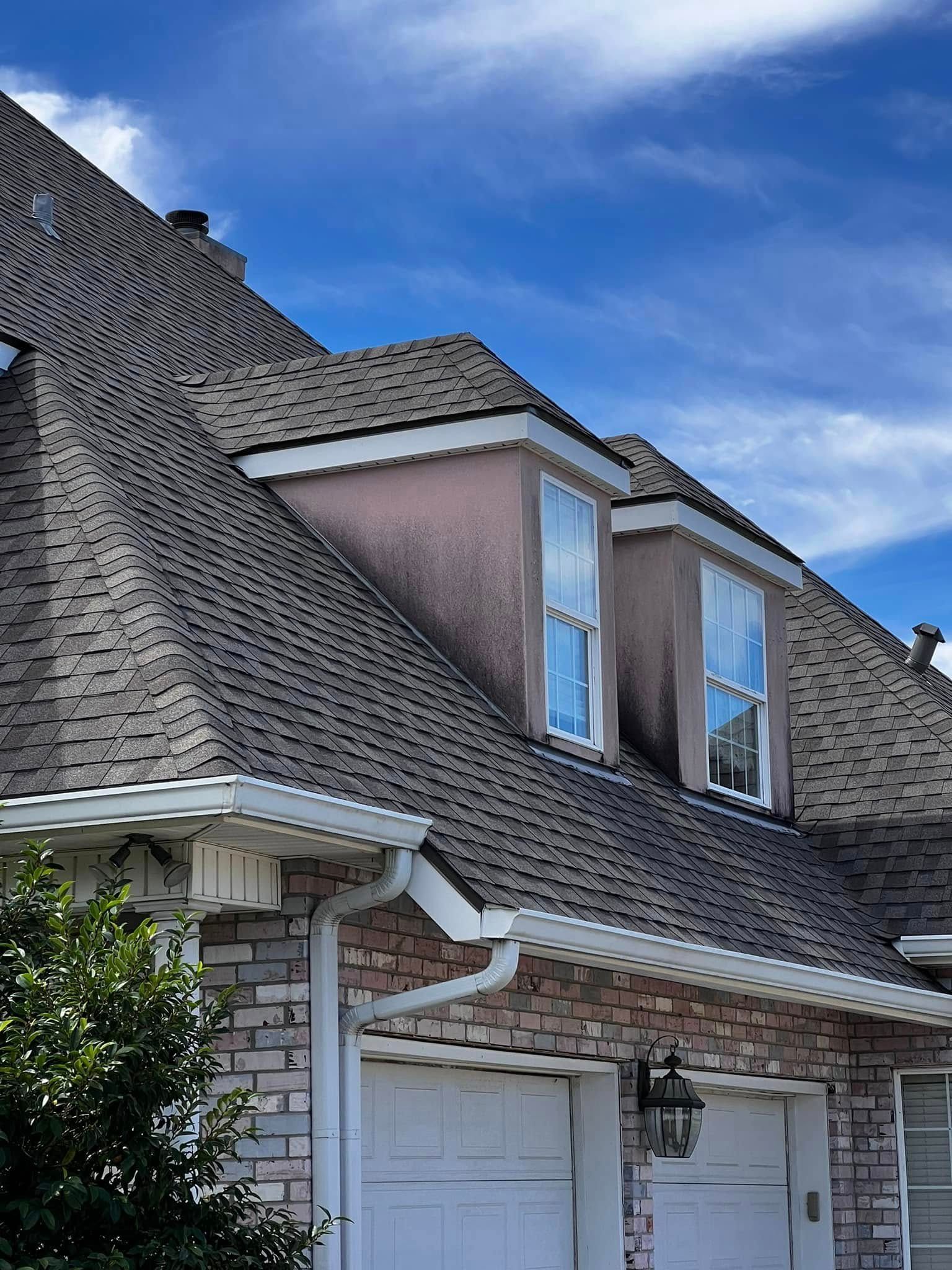 Suburban house with dark shingle roof, white garage, and dormer windows under a blue sky