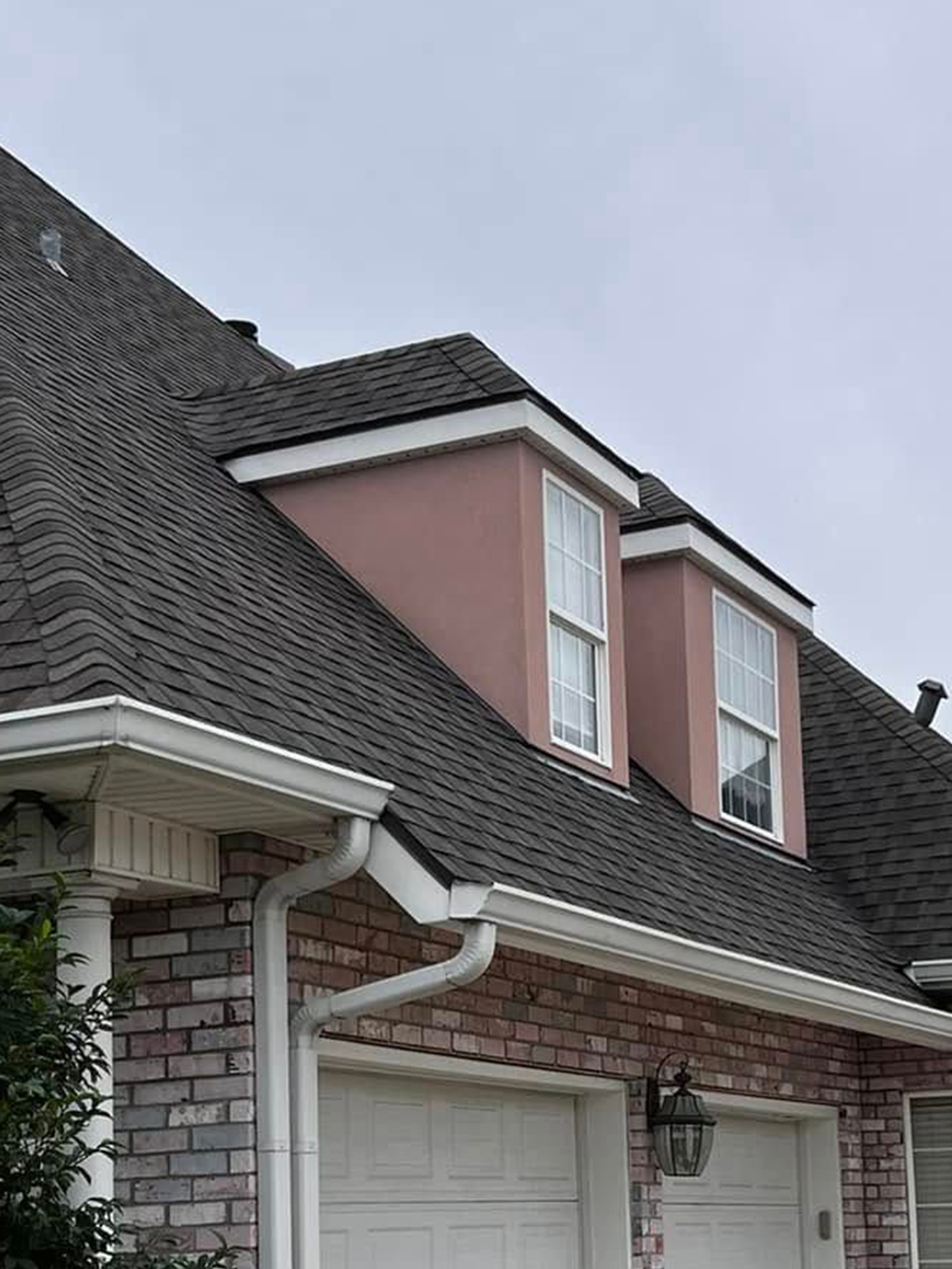 Suburban house with dark gray roof, pink dormer, and white garage beneath a covered entry