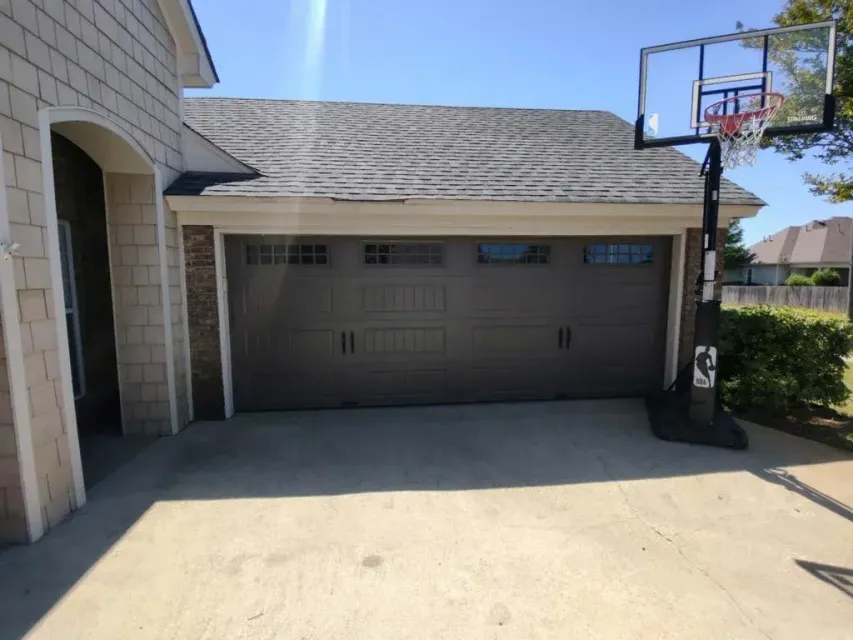 Garage with a basketball hoop in front. Grey door, brick accents, and light blue sky.