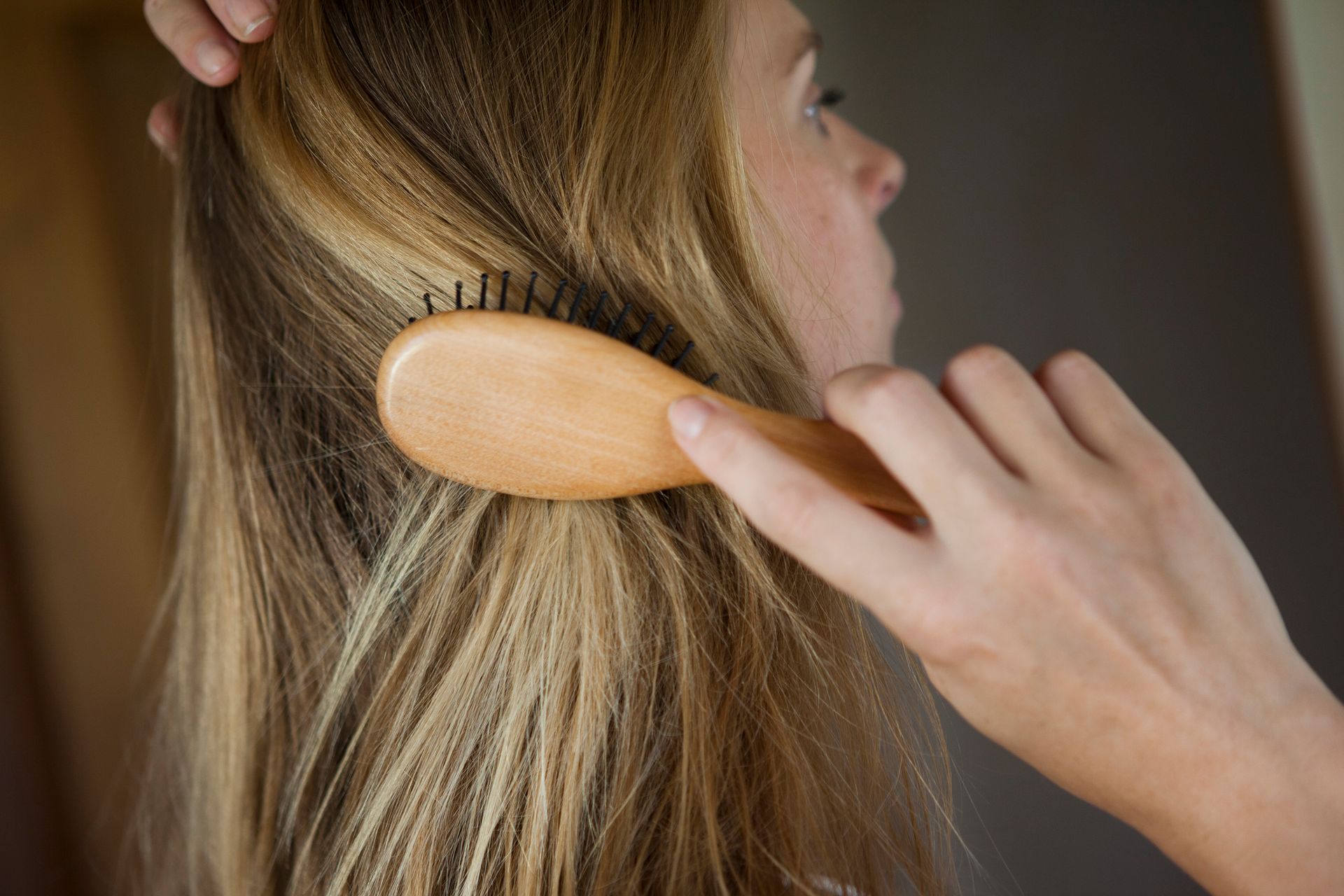 Una donna si spazzola i capelli con una spazzola di legno.
