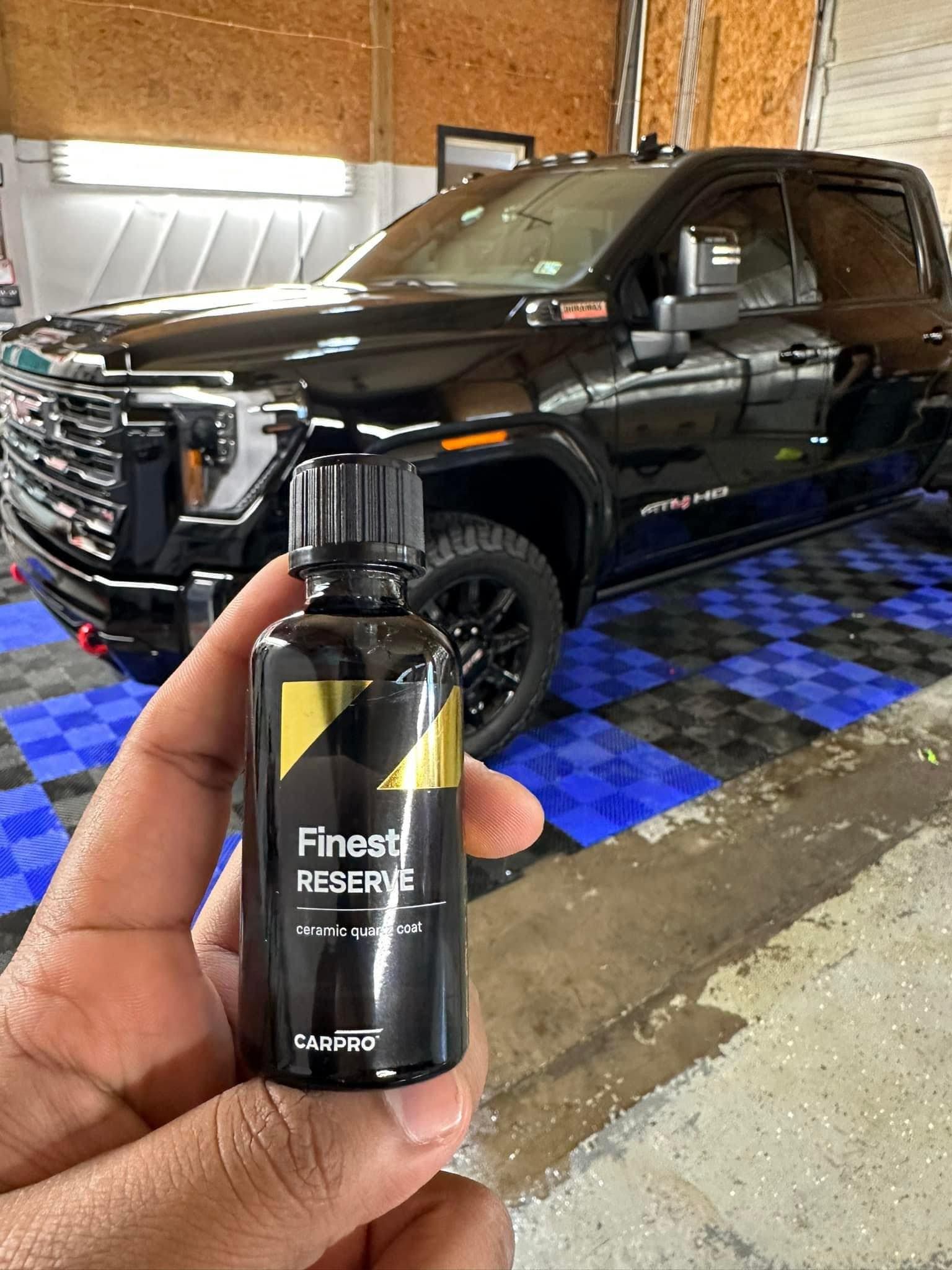Person holding a bottle of car detailing product with a black truck in the background.