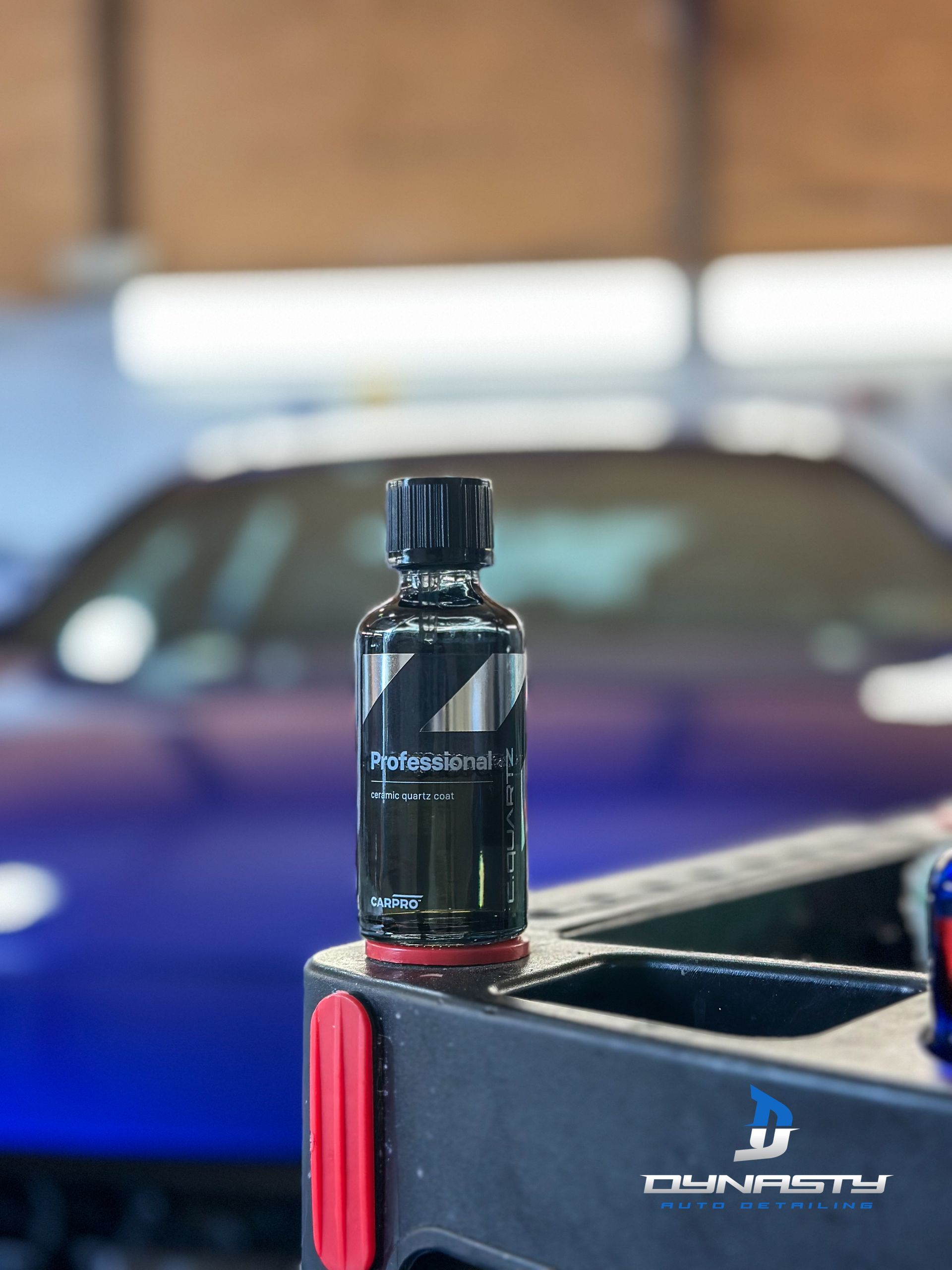 Black bottle of car ceramic coating on a cart with a blue car in the background.