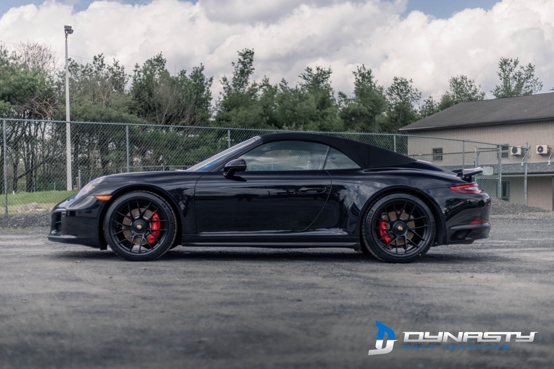 A black porsche 911 convertible is parked in a parking lot.