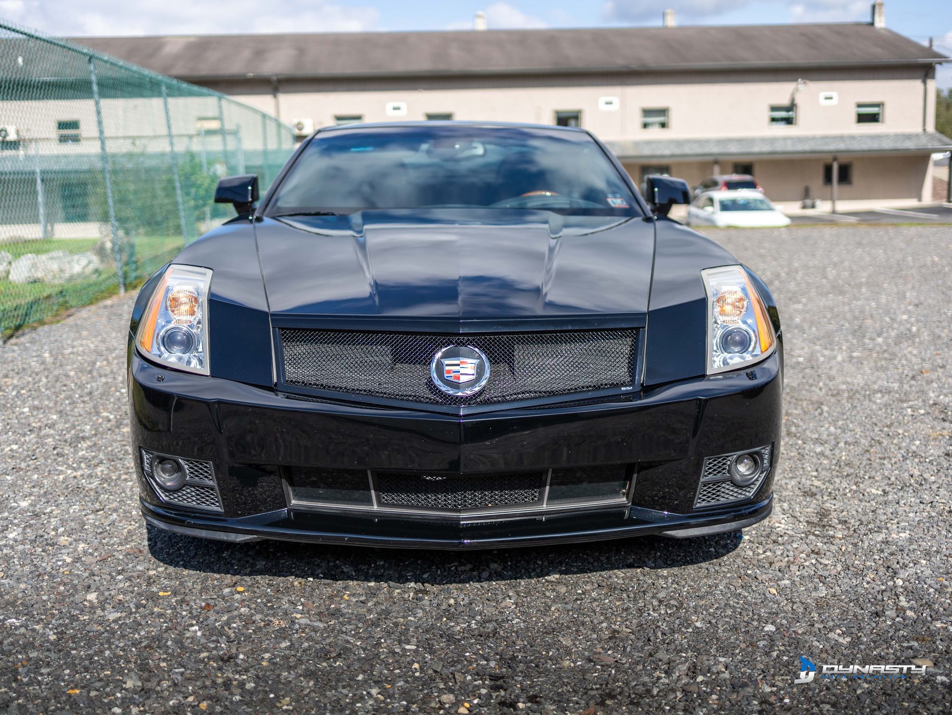 A black cadillac is parked in a gravel lot in front of a building.