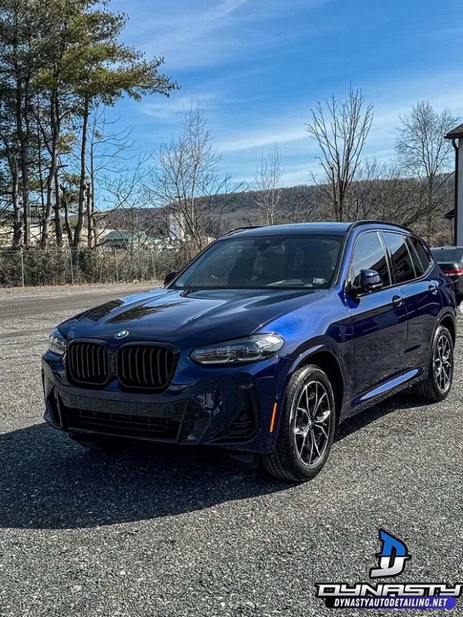 A blue bmw x3 is parked in a gravel lot.