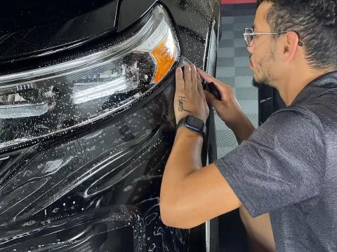 A man is wrapping a black car with plastic wrap.