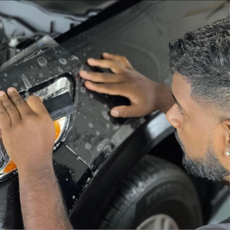 Person applying protective film to a black car's headlight with a squeegee.