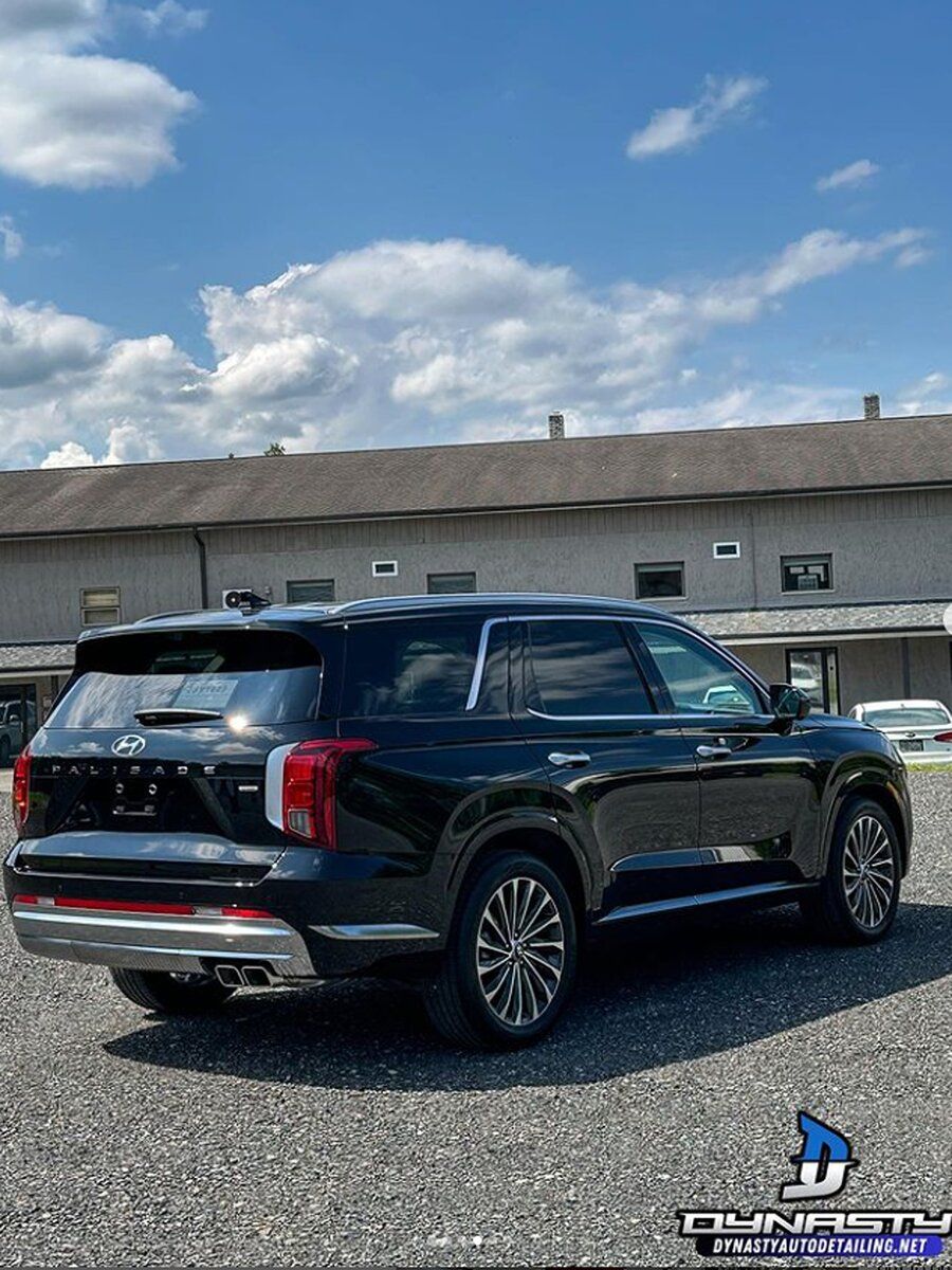 A black suv is parked in a gravel lot in front of a building.