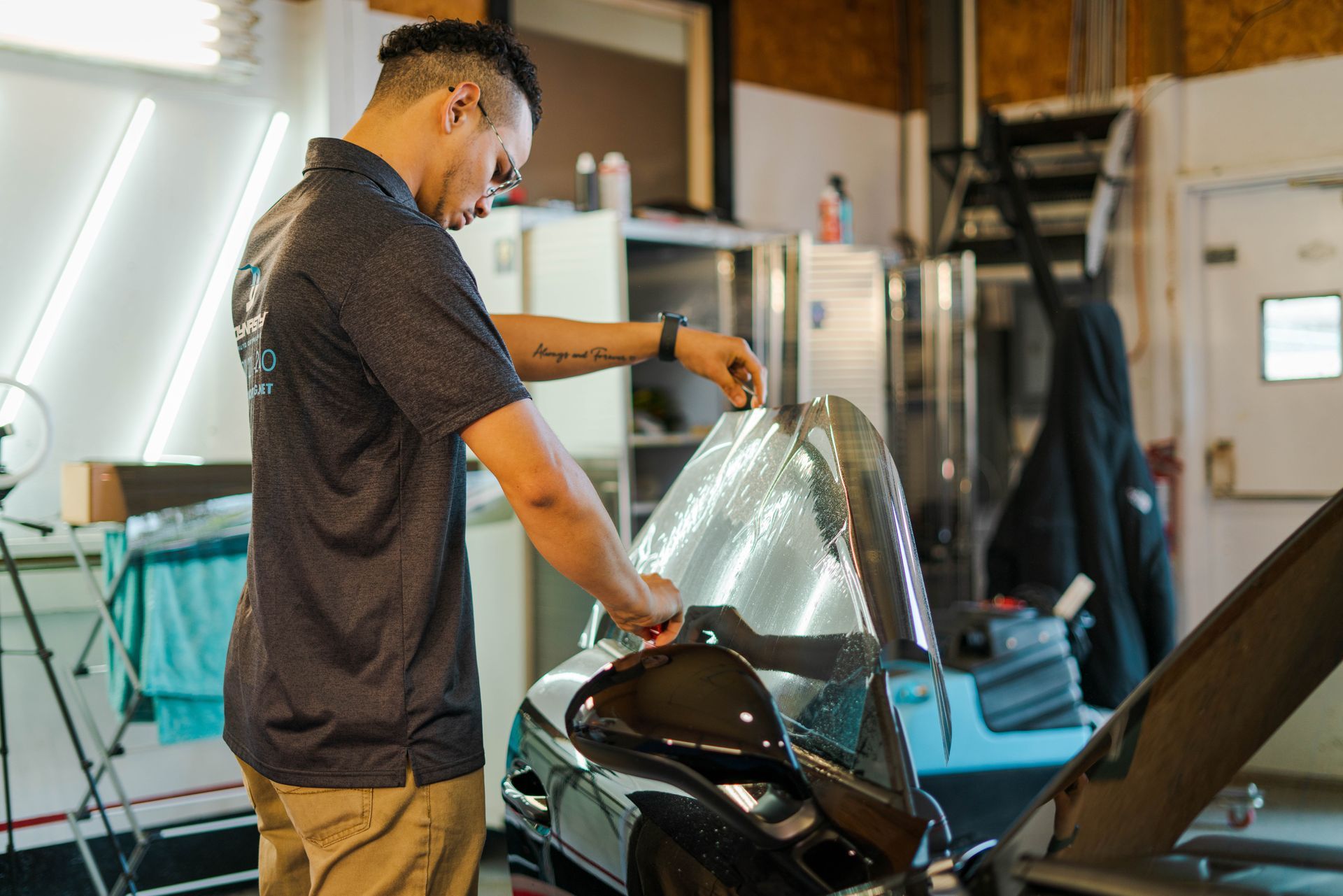 Man installing tint on a motorcycle windshield in a garage.