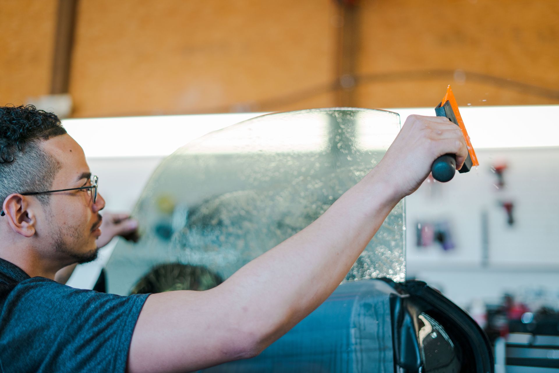 Person applying tint film to a car window with a squeegee in a workshop.