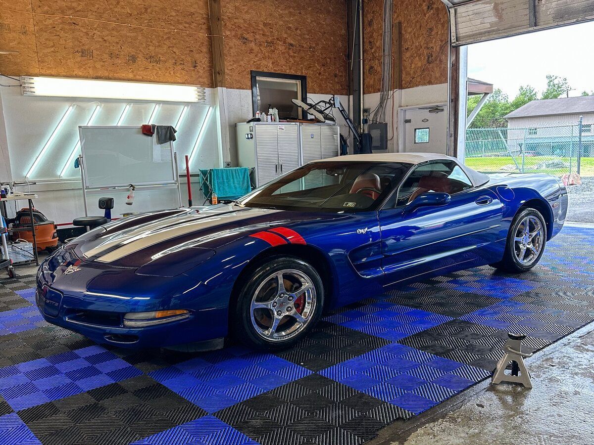Blue Chevrolet Corvette convertible in a garage with blue and black tiled flooring.