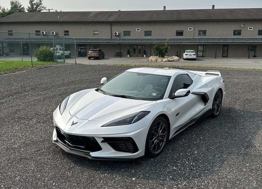 White Chevrolet Corvette sports car parked in front of a building on a gravel lot.