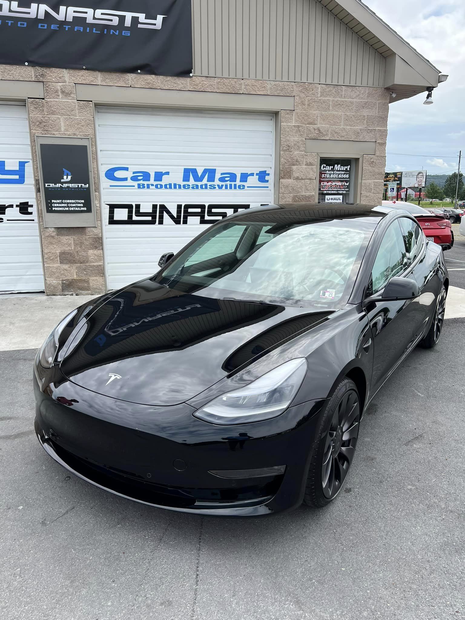 Black Tesla Model 3 parked in front of a car mart with a dynasty sign.
