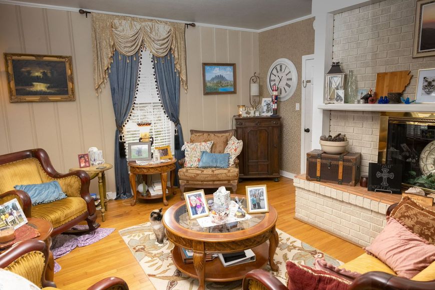 Vintage living room with floral sofa, round coffee table, fireplace, and blue drapes around a window