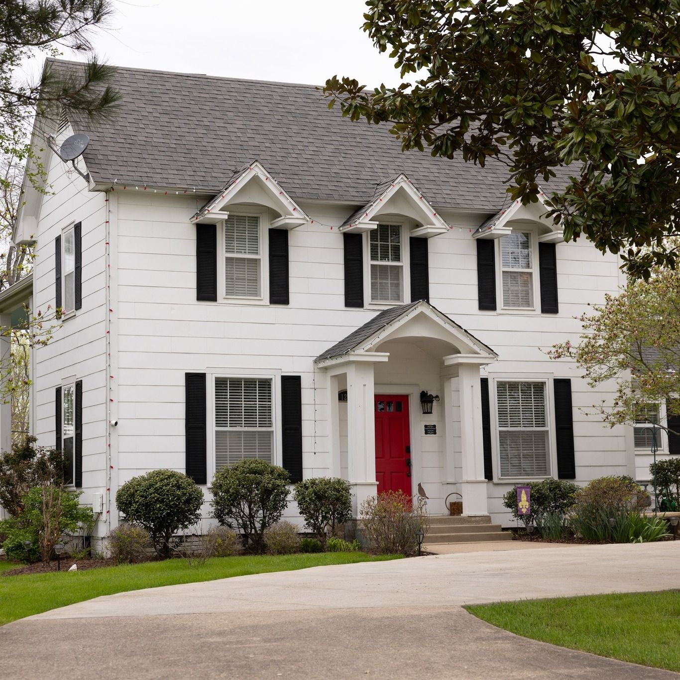 White two-story house with black shutters and a red front door, viewed from the driveway