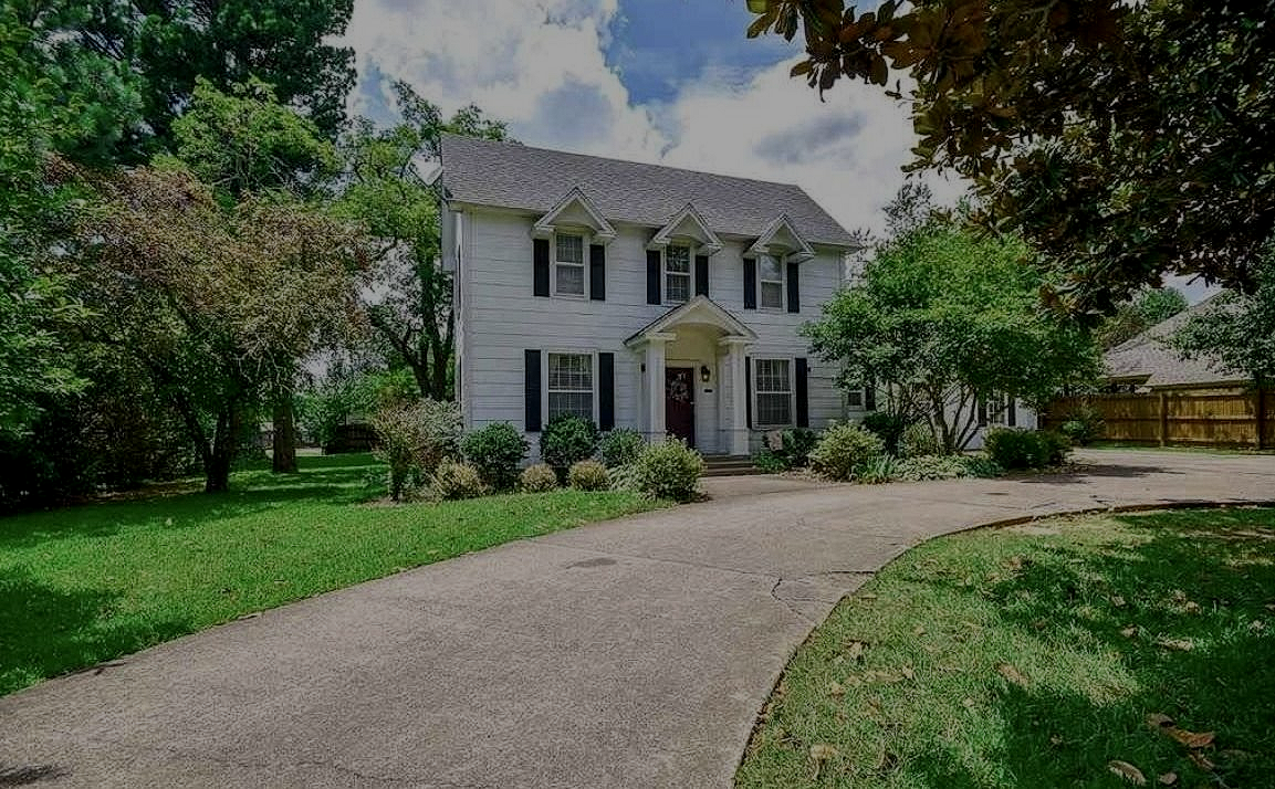 White two-story house with columns, framed by trees and a curved driveway on a sunny day