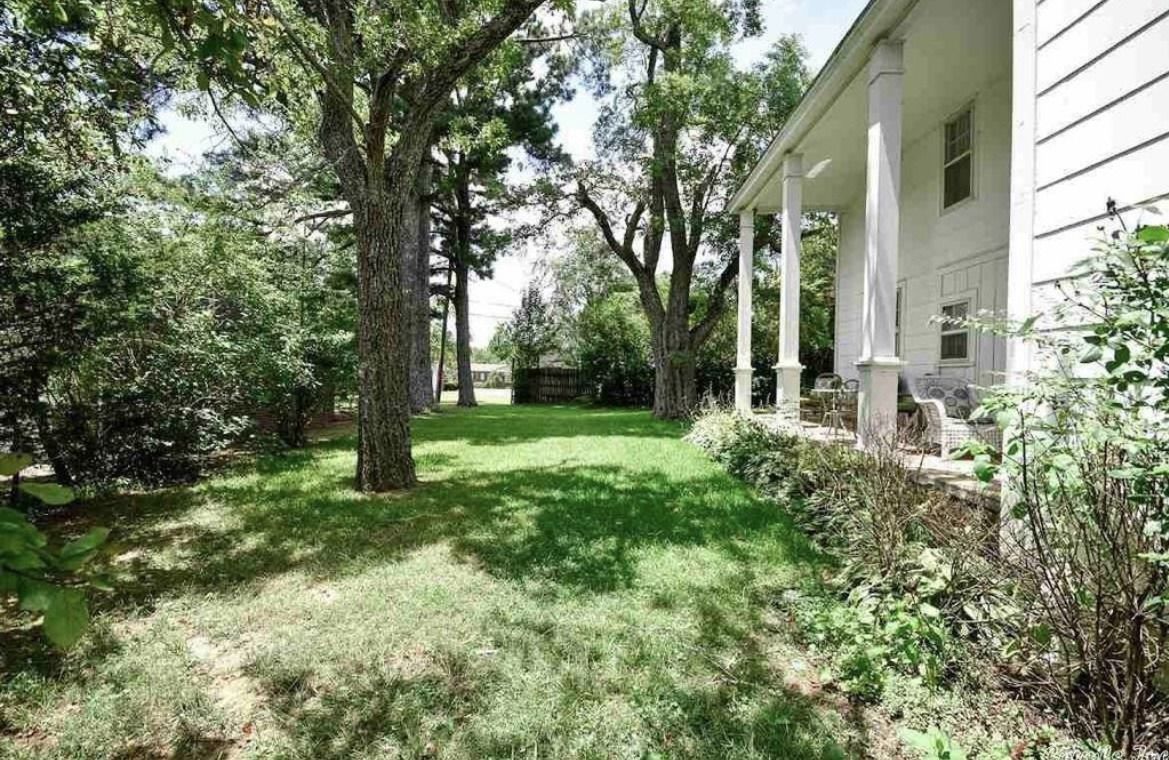 Shady backyard lawn beside a white house with trees and shrubs.