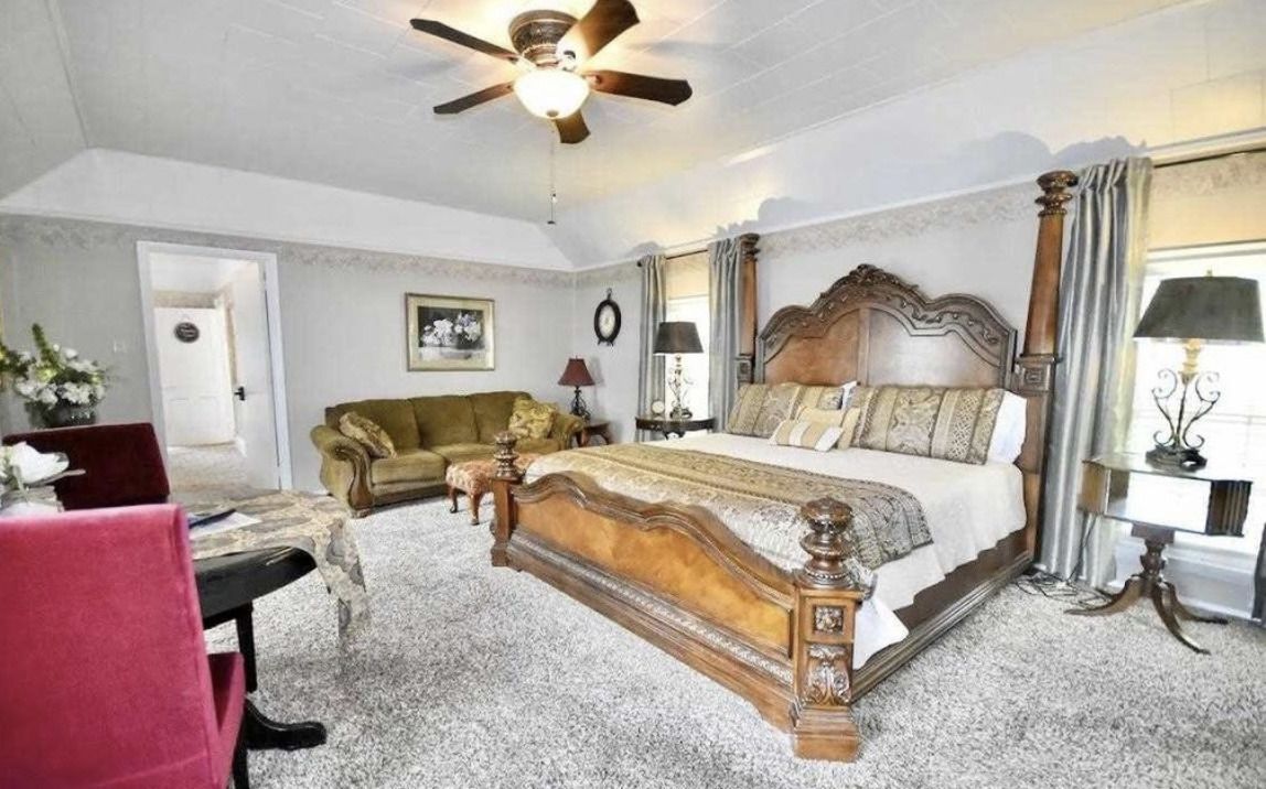 Spacious bedroom with ornate wooden bed, chandelier, gray curtains, and red accent chair