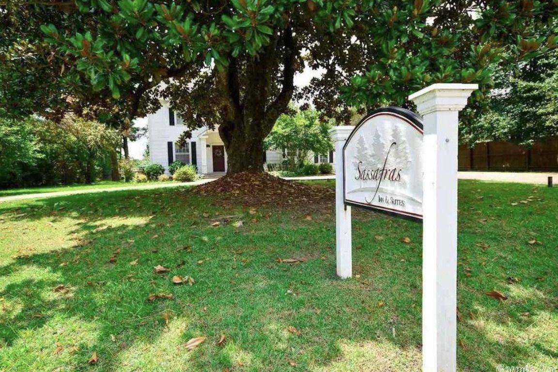 White church sign on a grassy lawn beneath a large tree, with a building in the background