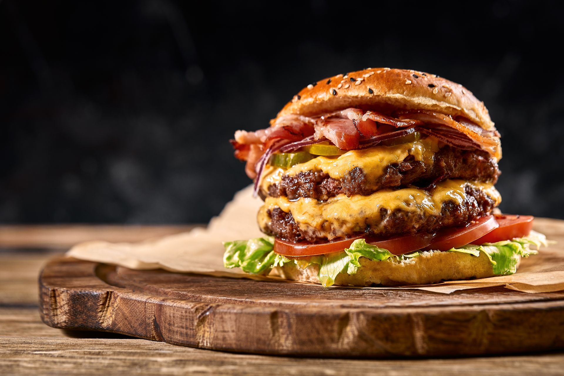 Juicy double cheeseburger with bacon and lettuce on a wooden board against a dark background