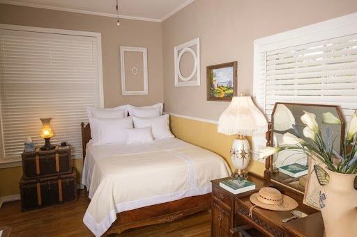 Neatly made bedroom with a white bed, beige walls, bedside tables, lamps, and framed wall art.