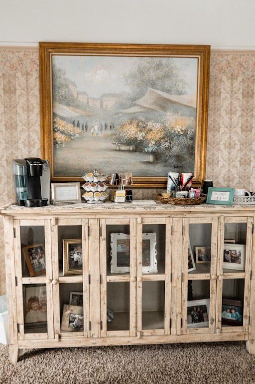 Rustic cabinet with framed landscape painting, coffee maker, and small decor on top in a home interior