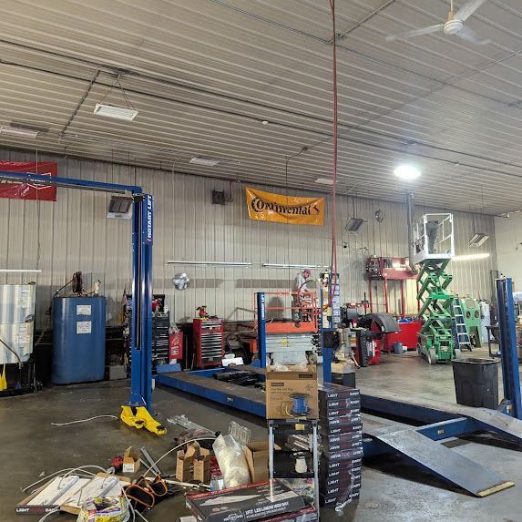 Auto repair shop interior with blue lift, tool carts, ramps, and scattered parts on the floor