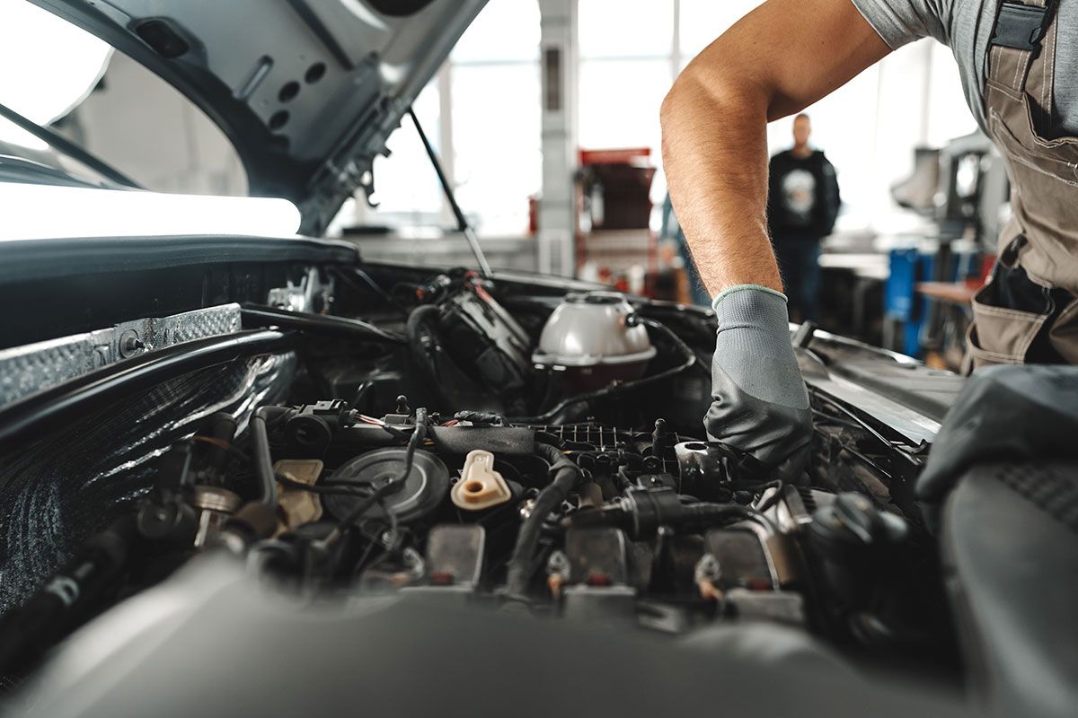 Mechanic working under an open car hood in an auto repair garage