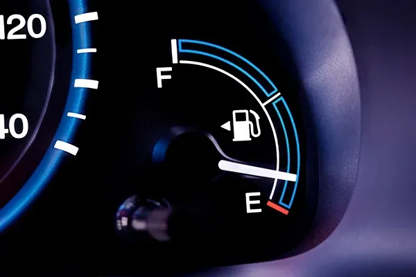 Car fuel gauge showing low fuel near E, with blue illuminated dashboard