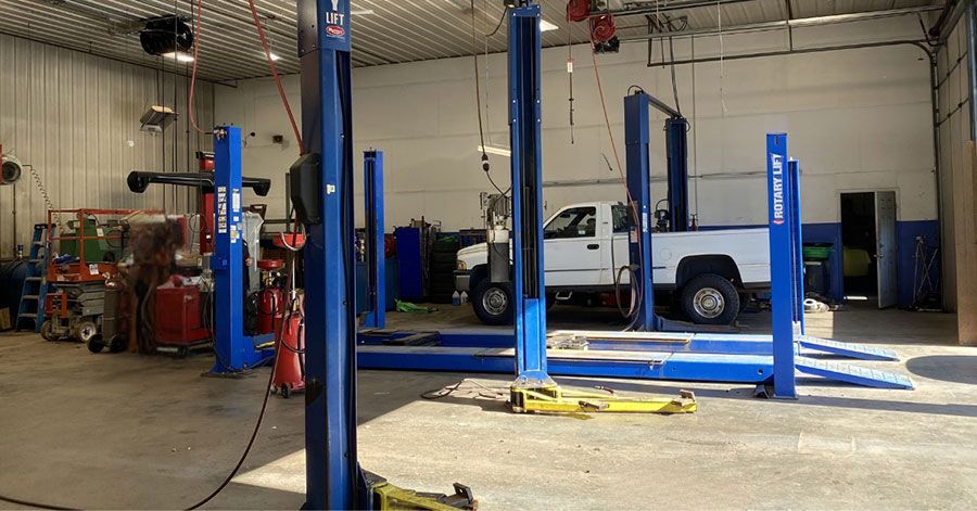 Auto repair shop interior with blue lift, tool carts, ramps, and scattered parts on the floor