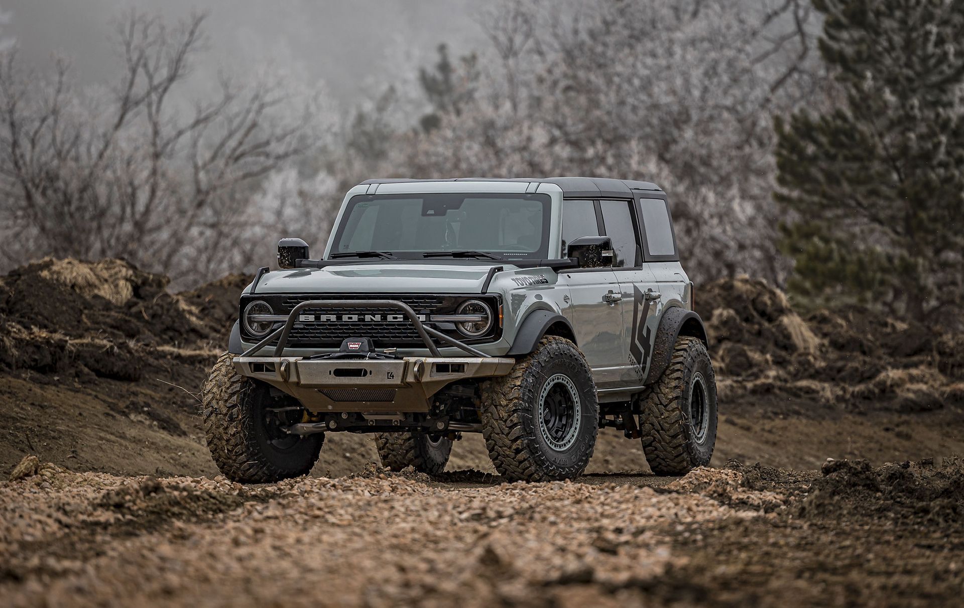 White off-road SUV in a muddy field with bare trees in the background