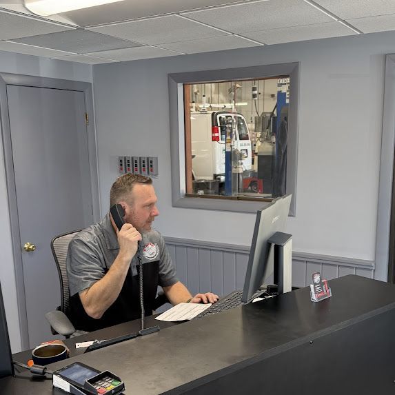 Man seated at a desk in an office, speaking on a phone and working at a computer.