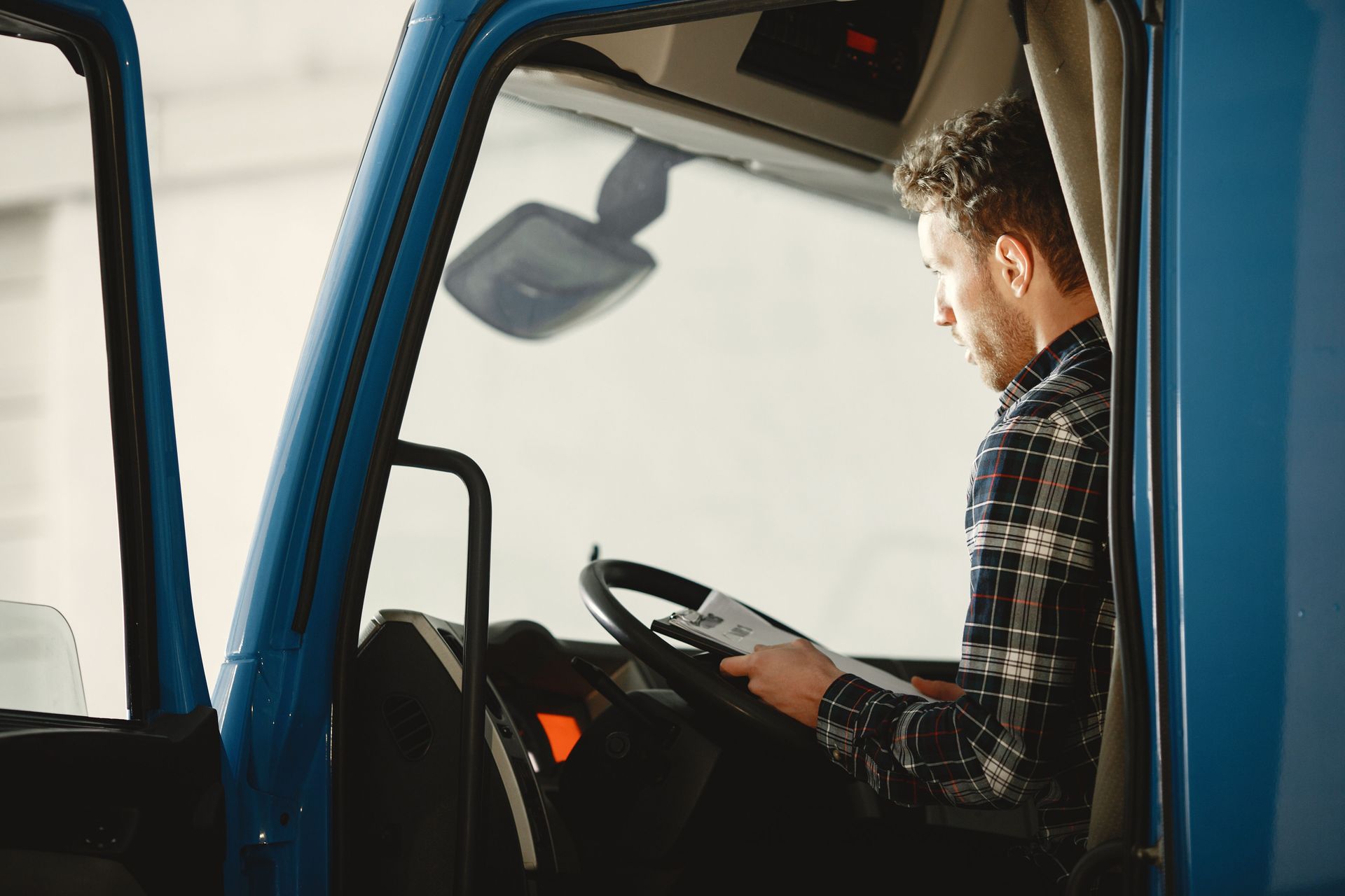Driver seated in a blue truck cab, holding the steering wheel and looking ahead