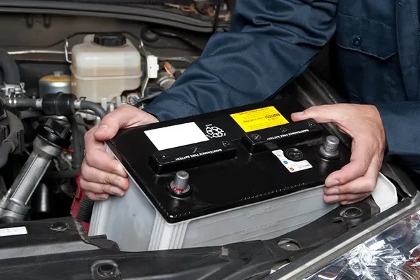 Hands installing a black car battery in an engine bay
