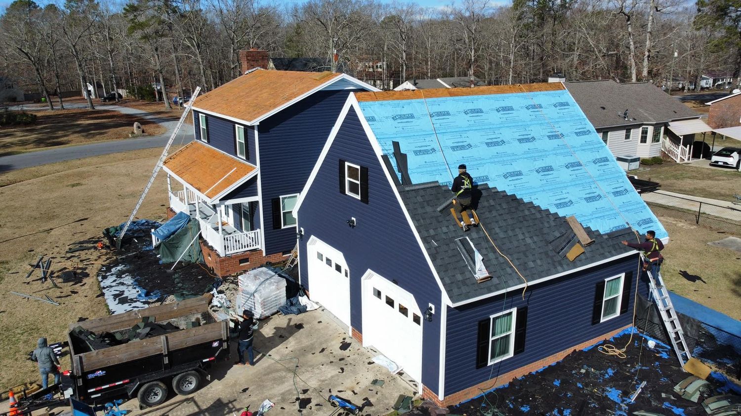 Blue house with a partially reroofed roof, covered in blue underlayment and construction debris around it.
