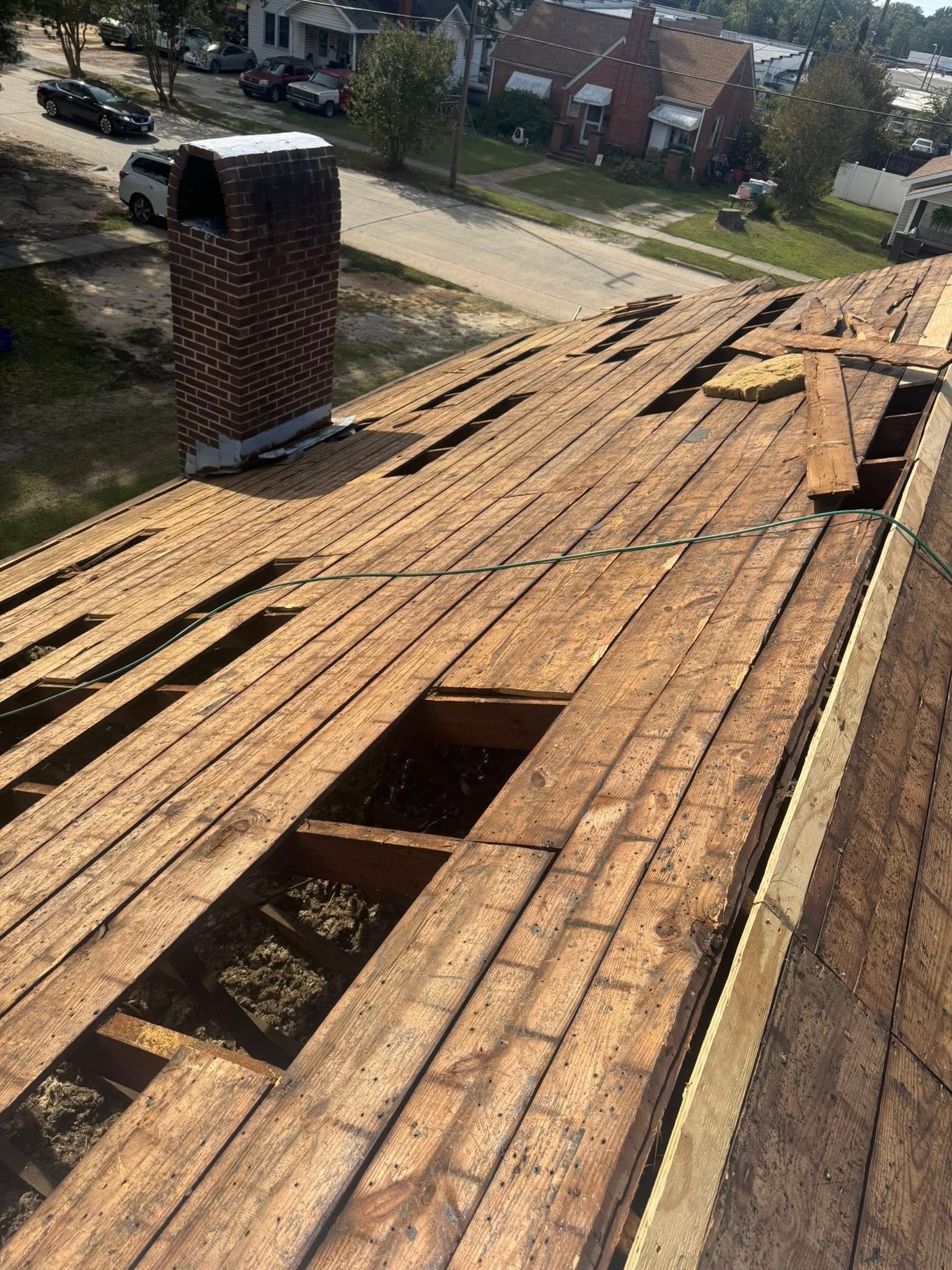 Damaged roof with missing shingles and exposed openings beside a chimney, viewed from above