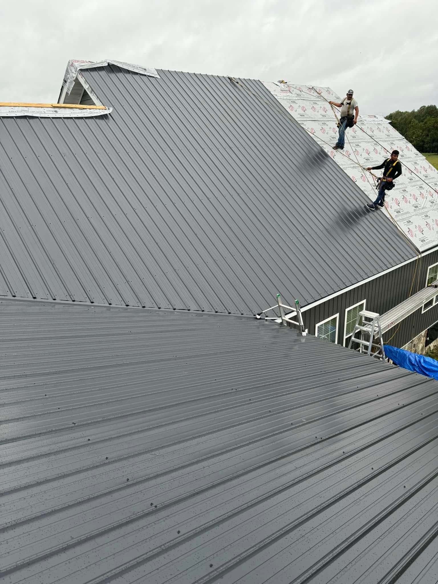 Two workers on a gray metal roof, inspecting a steep rooftop surface