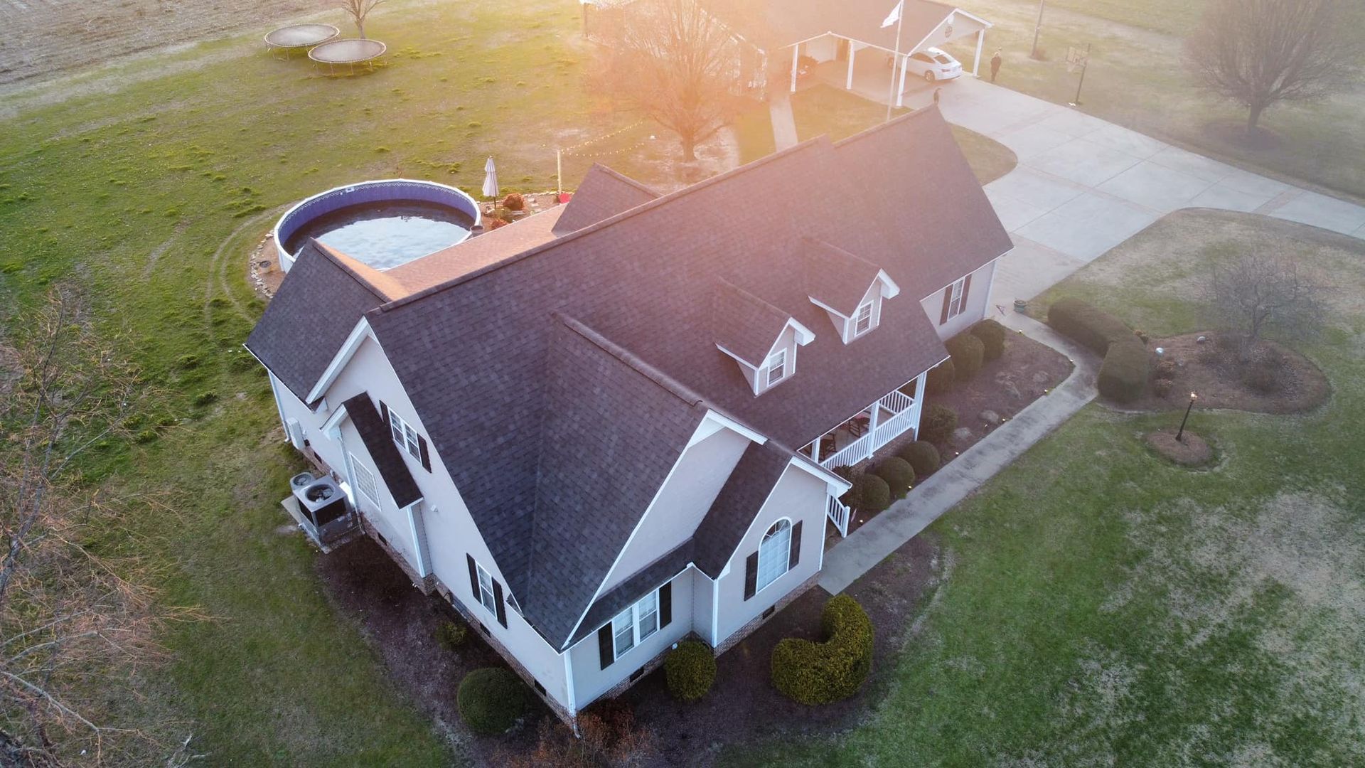 Aerial view of a large white house with a dark roof, driveway, and grassy yard at sunset.