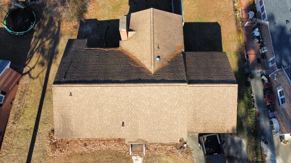 Aerial view of a tan house with a dark roof, backyard, and parked cars along a street.