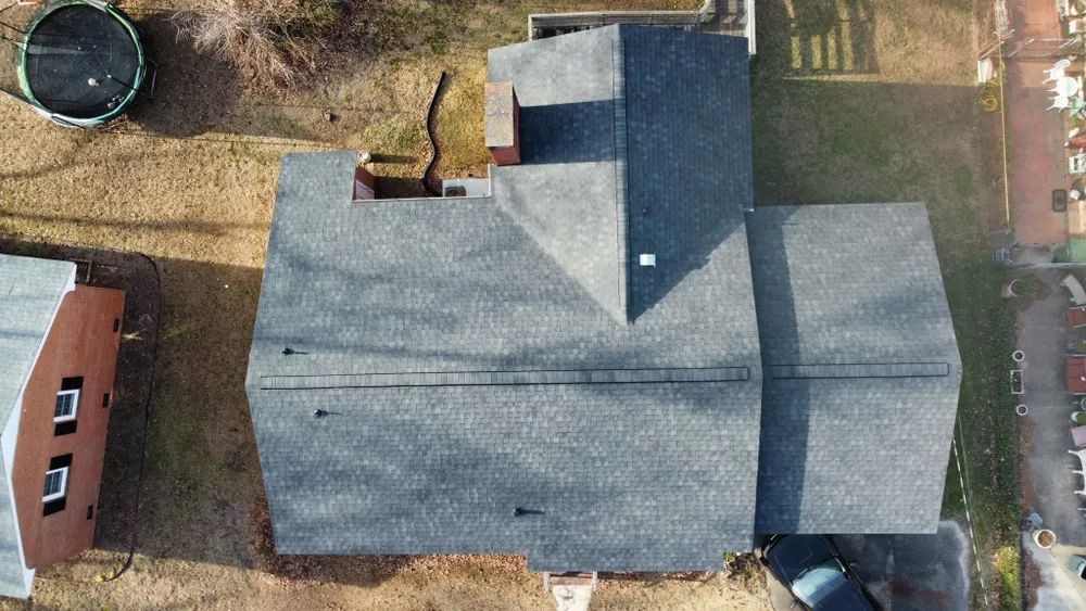 Overhead view of a gray-roofed house with a chimney and nearby trees and yard