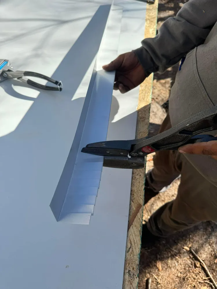 Person cutting a long white panel with snips on a workbench outdoors