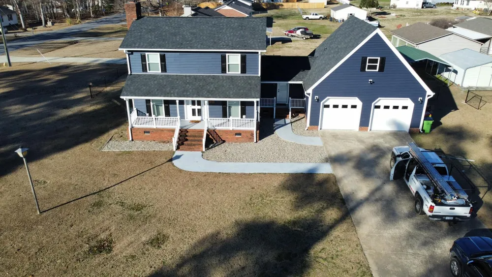 A two-story gray house with a detached garage, front porch, and a truck parked in the driveway.