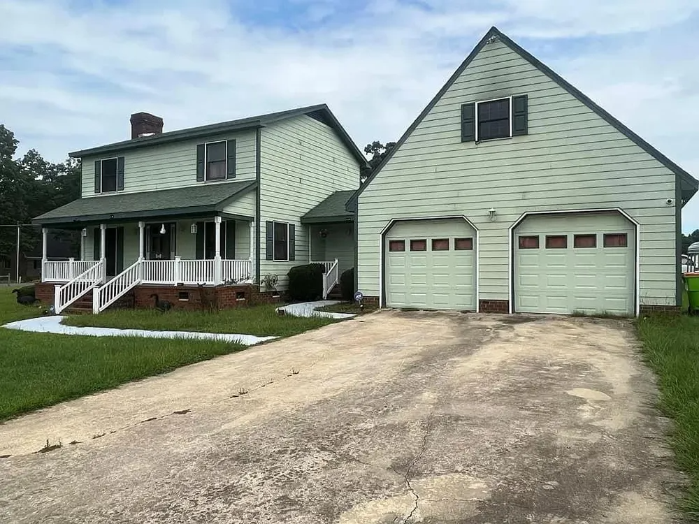 Two-story house with green siding, attached two-car garage, and a gravel driveway