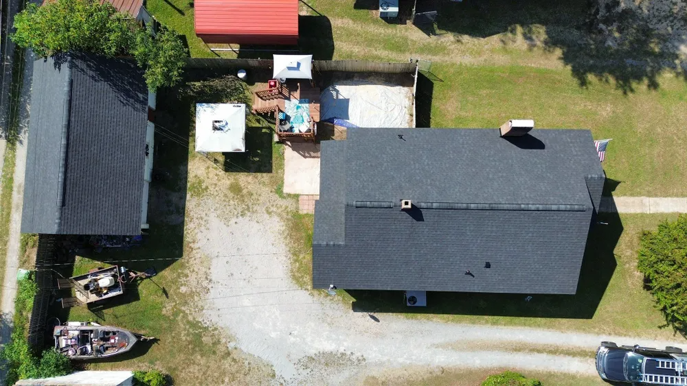 Aerial view of a house, driveway, yard, and small dock with boats beside a waterfront.