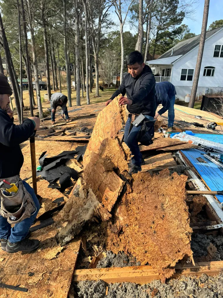 Workers dismantling a large fallen tree trunk beside a house in a wooded yard