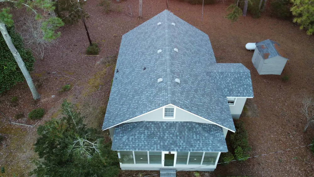 Aerial view of a white house with a gray roof surrounded by trees and a small outbuilding.