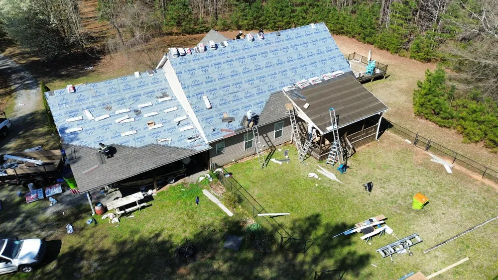 Aerial view of a house with a damaged roof and scattered debris in a grassy yard