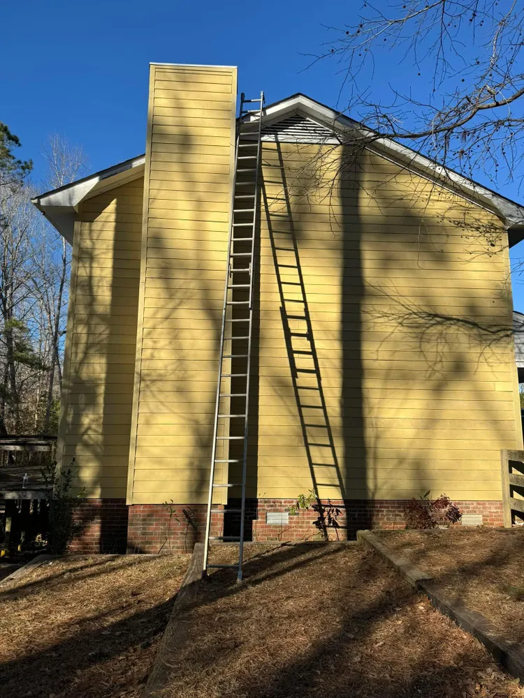 Yellow house exterior with tall central chimney and a ladder leaning against the roofline